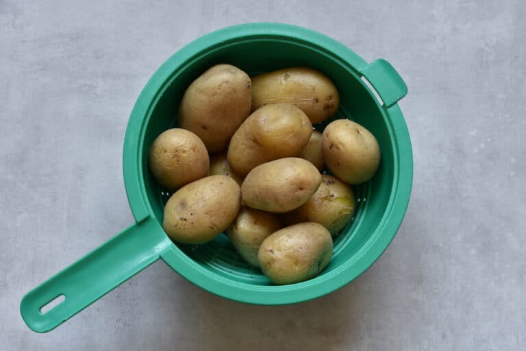 Potatoes boiled with their skins on steam drying in a colander.