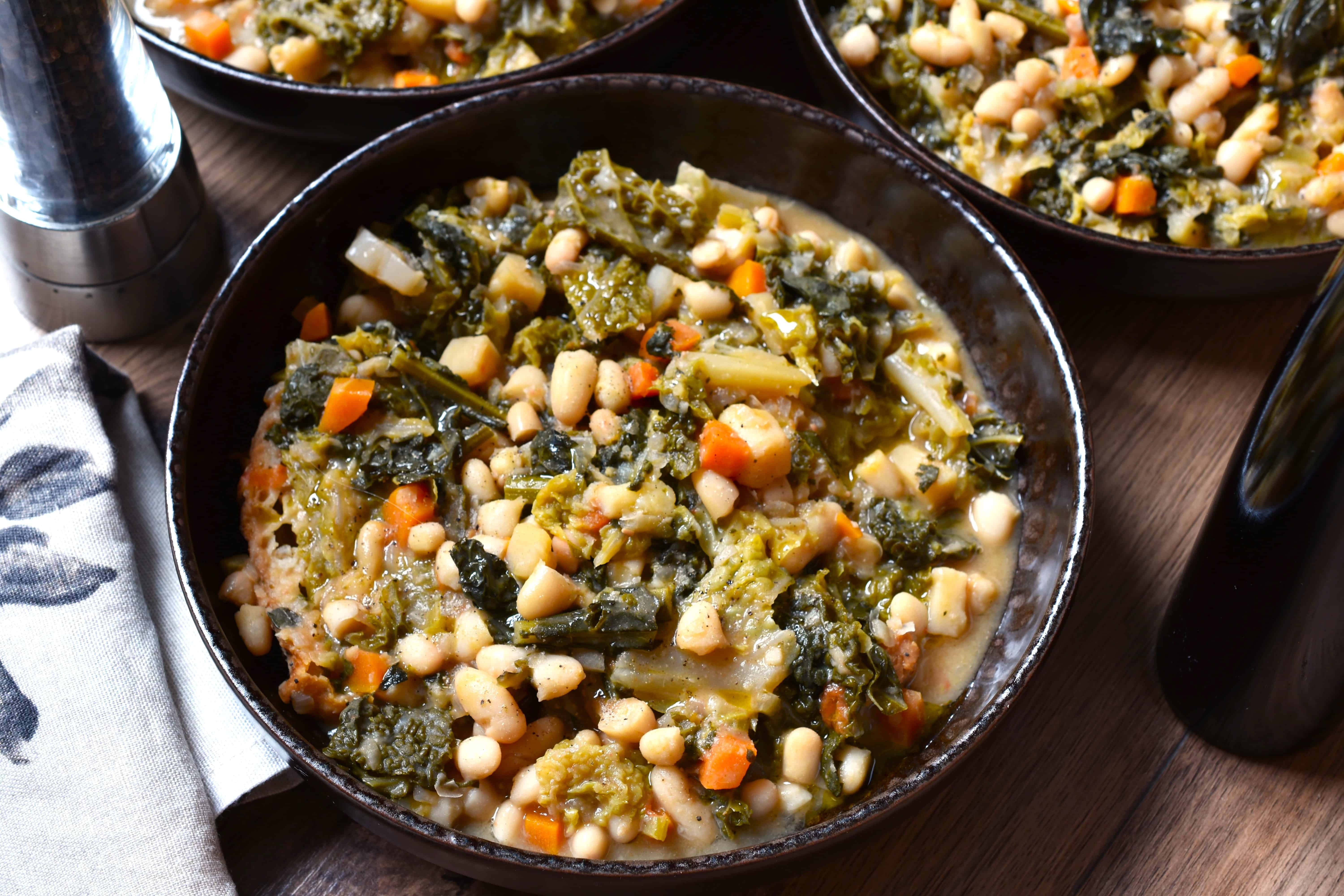 Three plates of ribollita toscana (Tuscan ribollita) on a table with kitchen cloths , a bottle of extra virgin olive oil and a pepper mill.