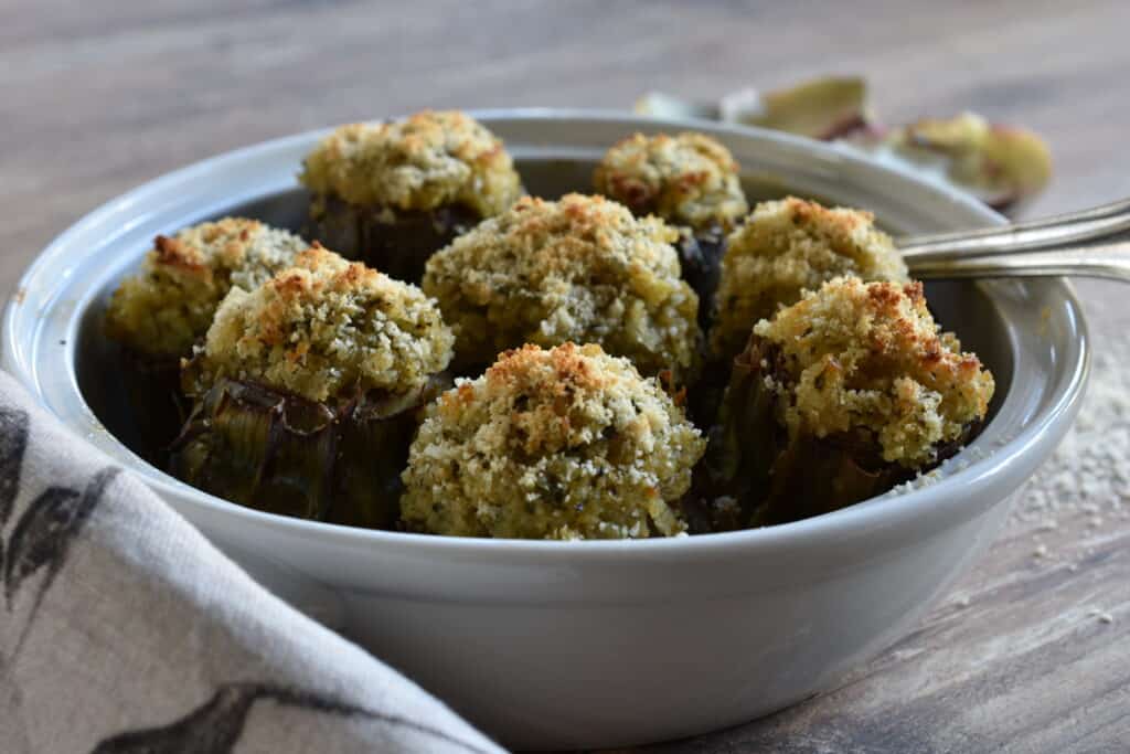 Stuffed artichokes in a white oven dish with a spoon and fork and cloth.