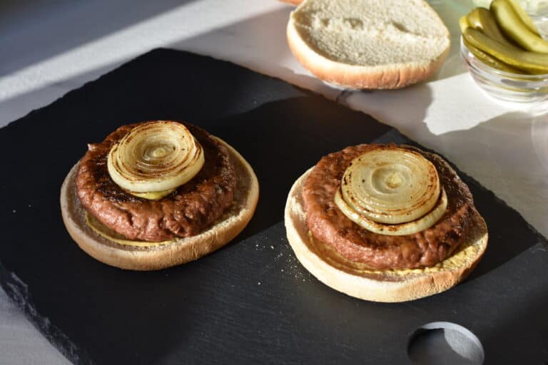 Toasted vegan burger buns with mustard, a vegan fast food burger and fried onions.