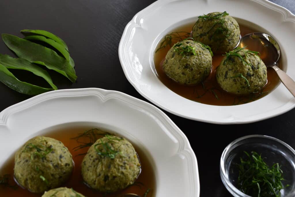 Two soup plates of vegan wild garlic bread dumplings (canederli) in vegetable broth.