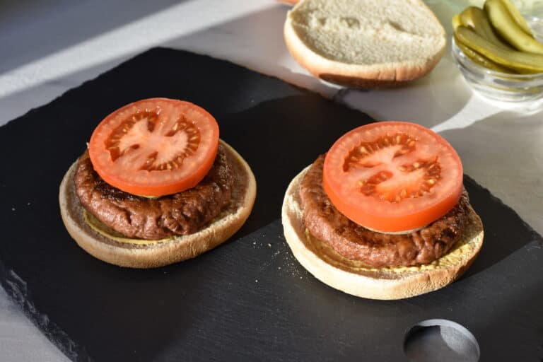 Vegan burger bun bottons with a vegan fast food burger, fried onion and a slice of tomato.