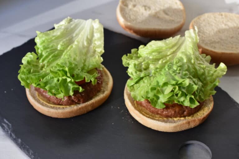 Vegan burger buns with mustard, vegan fast food burger, onions, tomato, gherkin and lettuce.