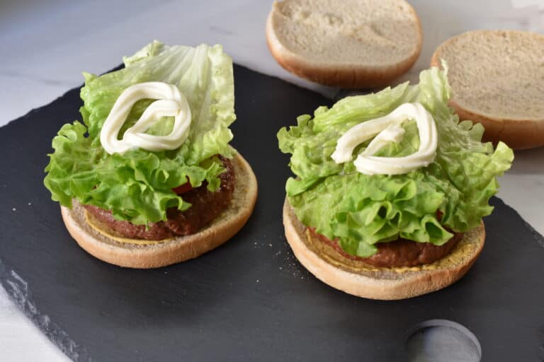 Vegan burger buns with mustard, vegan fast food burger, onions, tomato, gherkin, lettuce and mayonnaise.