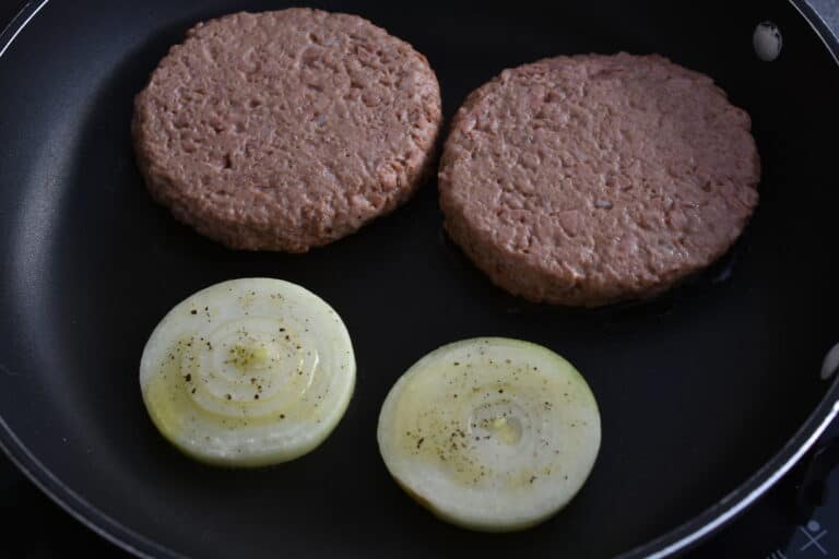 Vegan fast food burgers and onion slices in a frying pan.