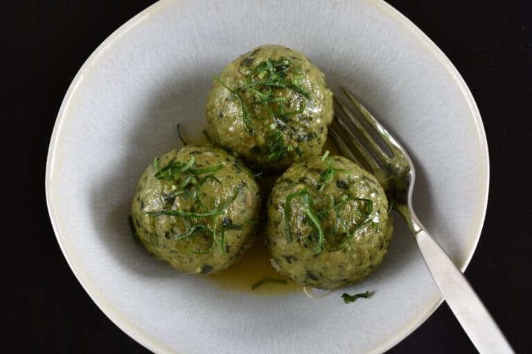 Vegan wild garlic bread dumplings (canederli) with melted vegan butter in a bowl with a fork.