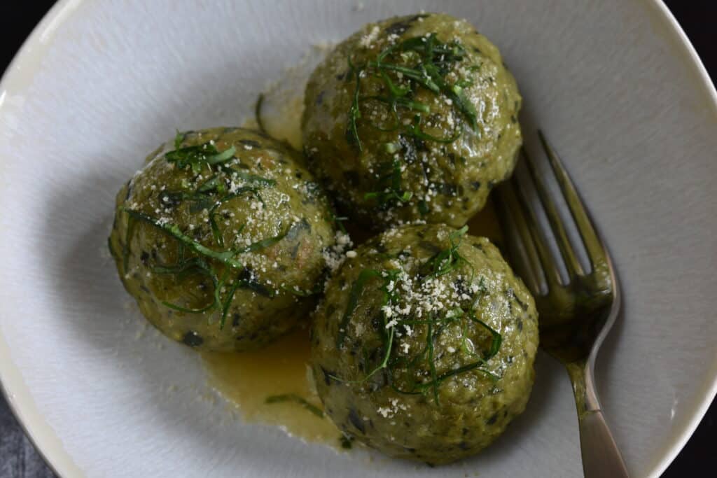 Vegan wild garlic dumplings (canederli) with melted vegan butter and vegan parmesan cheese in a white bowl with a fork.