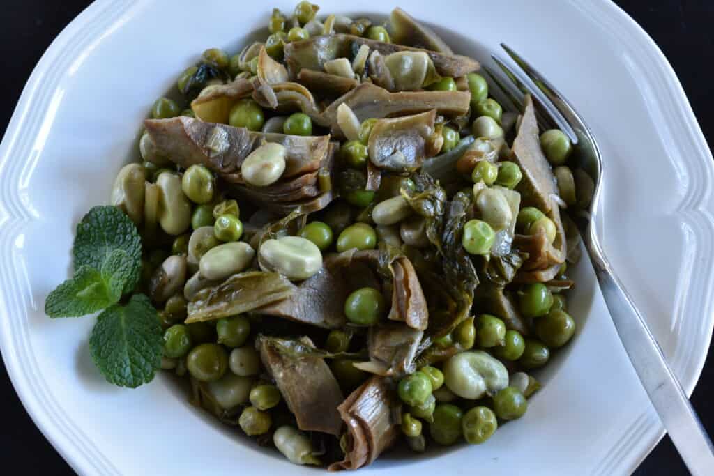 Vignarola on a white plate with a fork and a garnish of fresh mint.