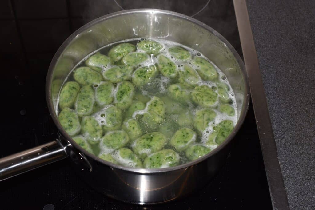 Wild garlic gnocchi floating in a pan of boiling water.