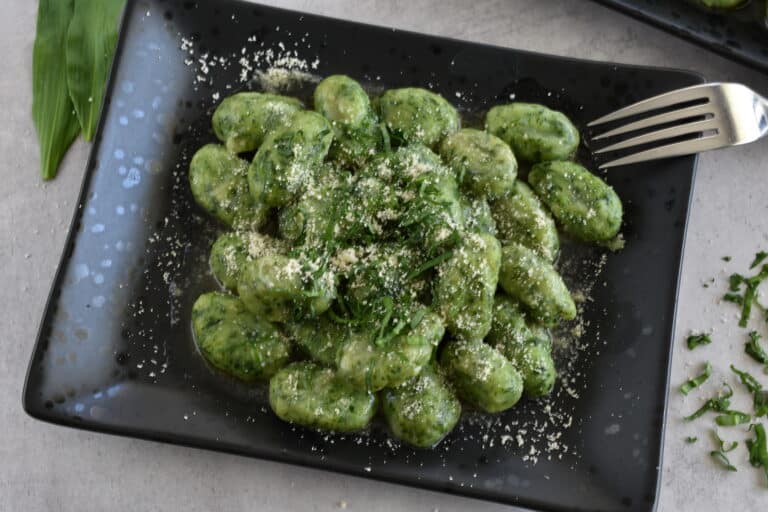 Wild garlic (ramsons) gnocchi on a black plate with a sprinkling of vegan parmesan cheese.