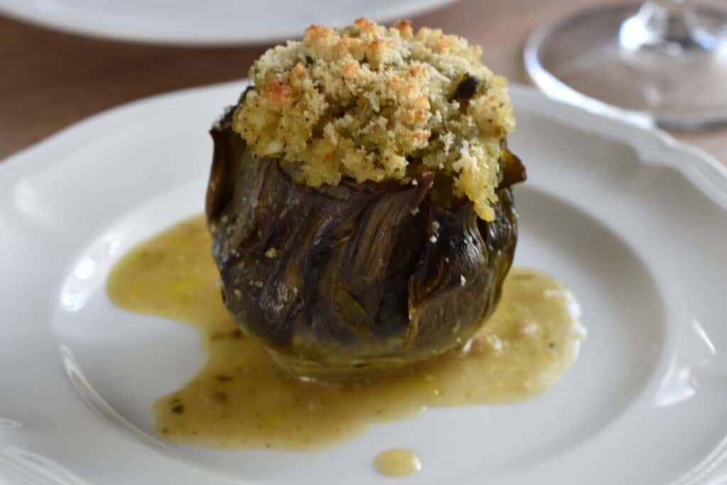 A close-up image of a stuffed artichoke on a white plate.