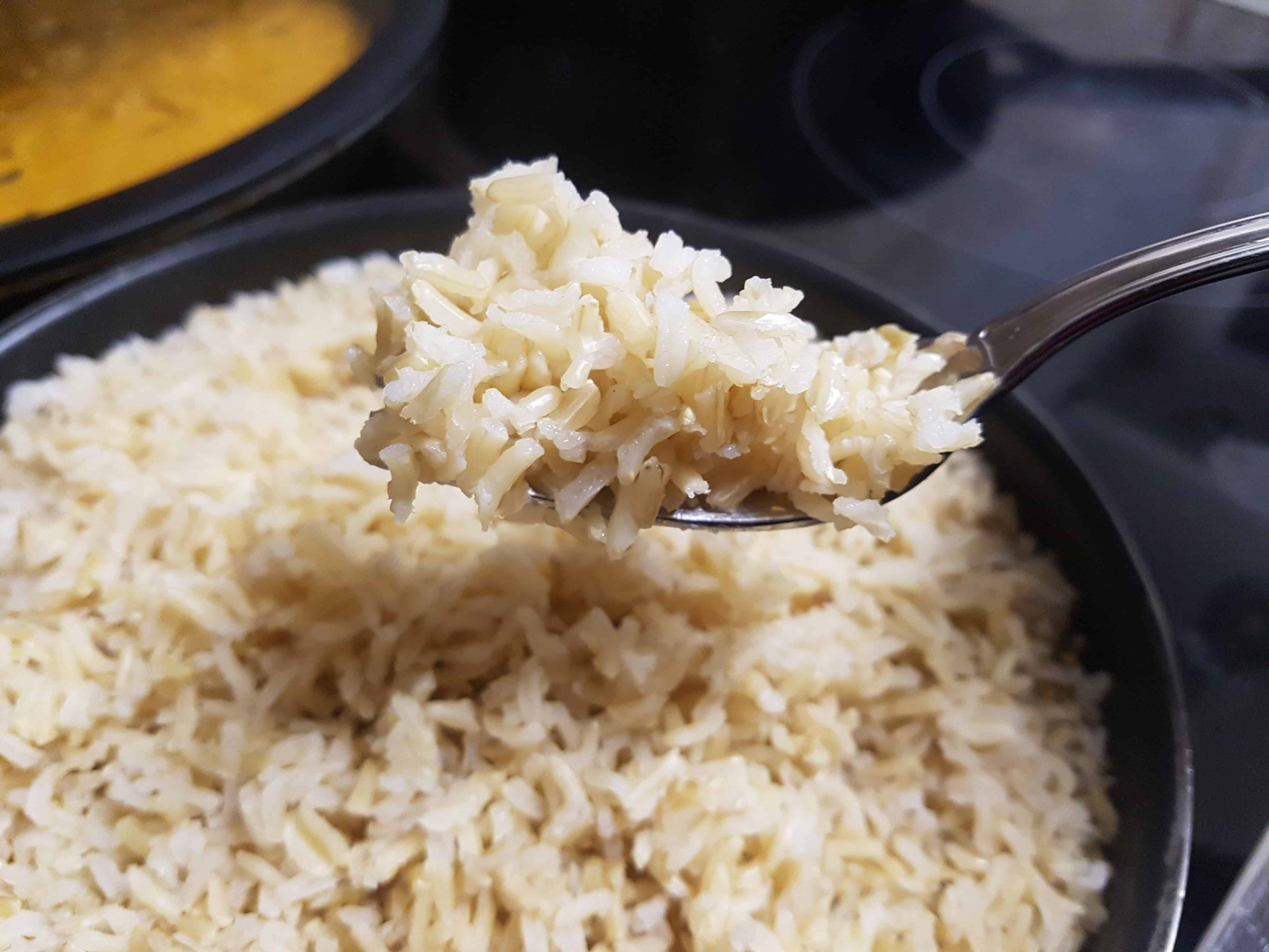 A forkful of fluffy brown basmati rice being held over a pan.