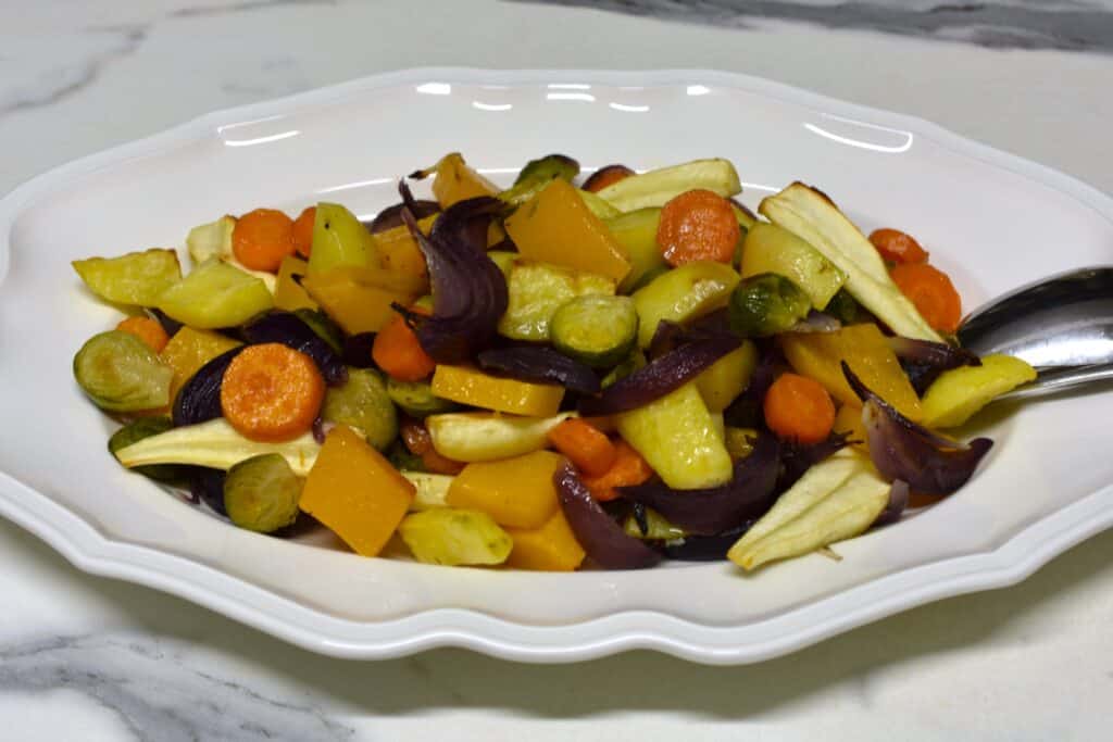 Oven-roasted winter vegetables on a white plate with a spoon and fork