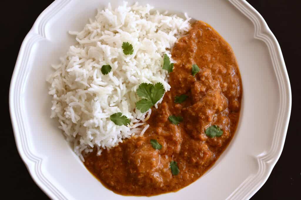 Overhead view of vegan chicken tikka masala with white basmati rice on a white plate.