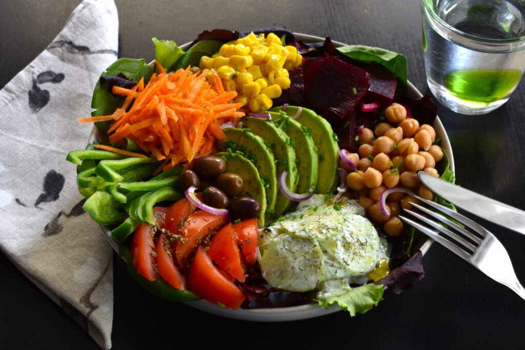 Rainbow mixed salad bowl with a serviette, knife and fork, and a glass of water on a table.