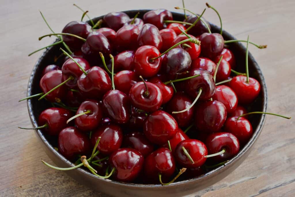 A bowl of Italian vignola cherries in a brown dish on a wooden table.