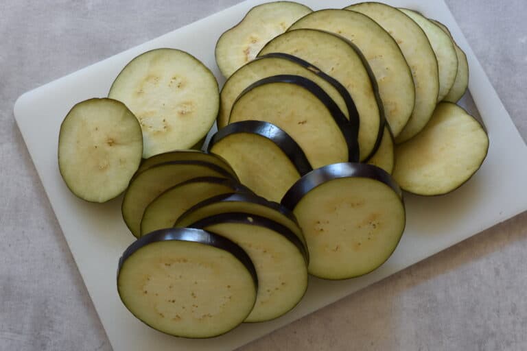 1 cm thick aubergine slices on a chopping board on a kitchen work top.