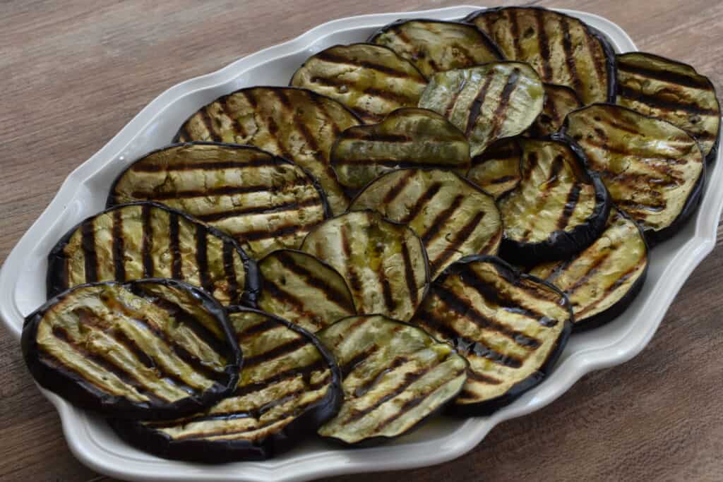 Grilled aubergines on an oval serving platter on a wooden table.