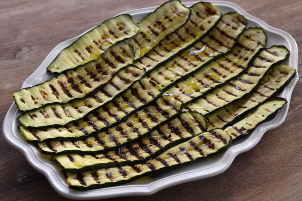 Grilled courgettes (zucchini) seasoned with salt and extra virgin olive oil on a white oval serving platter.