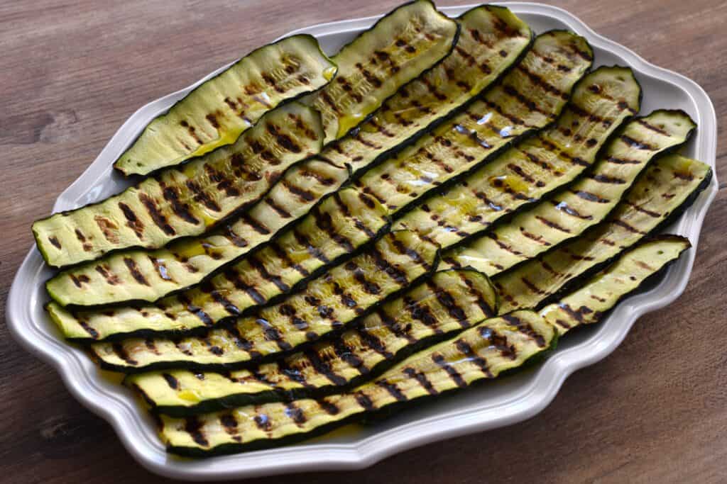 Grilled courgettes (zucchini) on an oval serving platter seasoned with salt and extra virgin olive oil.