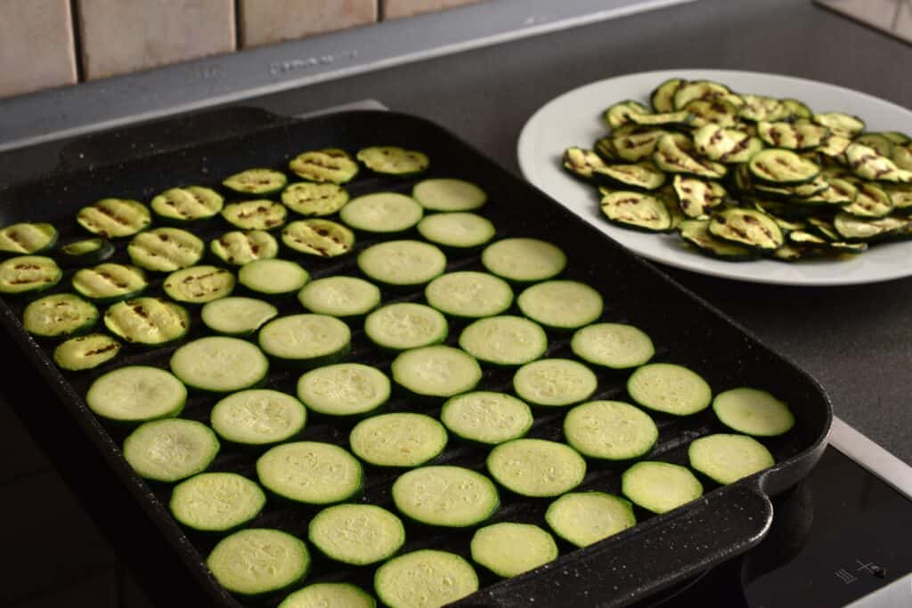 Grilling courgette rounds on a grill pan and on a plate to the side.