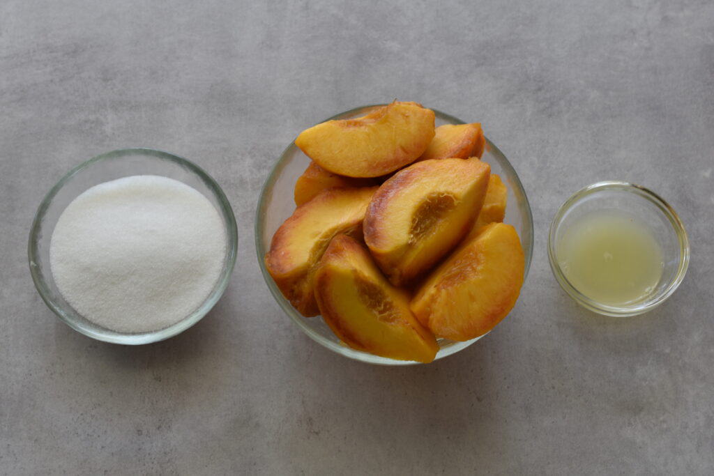 Ingredients for peach sorbet (fresh skinned peach quarters, vegan white sugar, and lemon juice) in glass bowls.