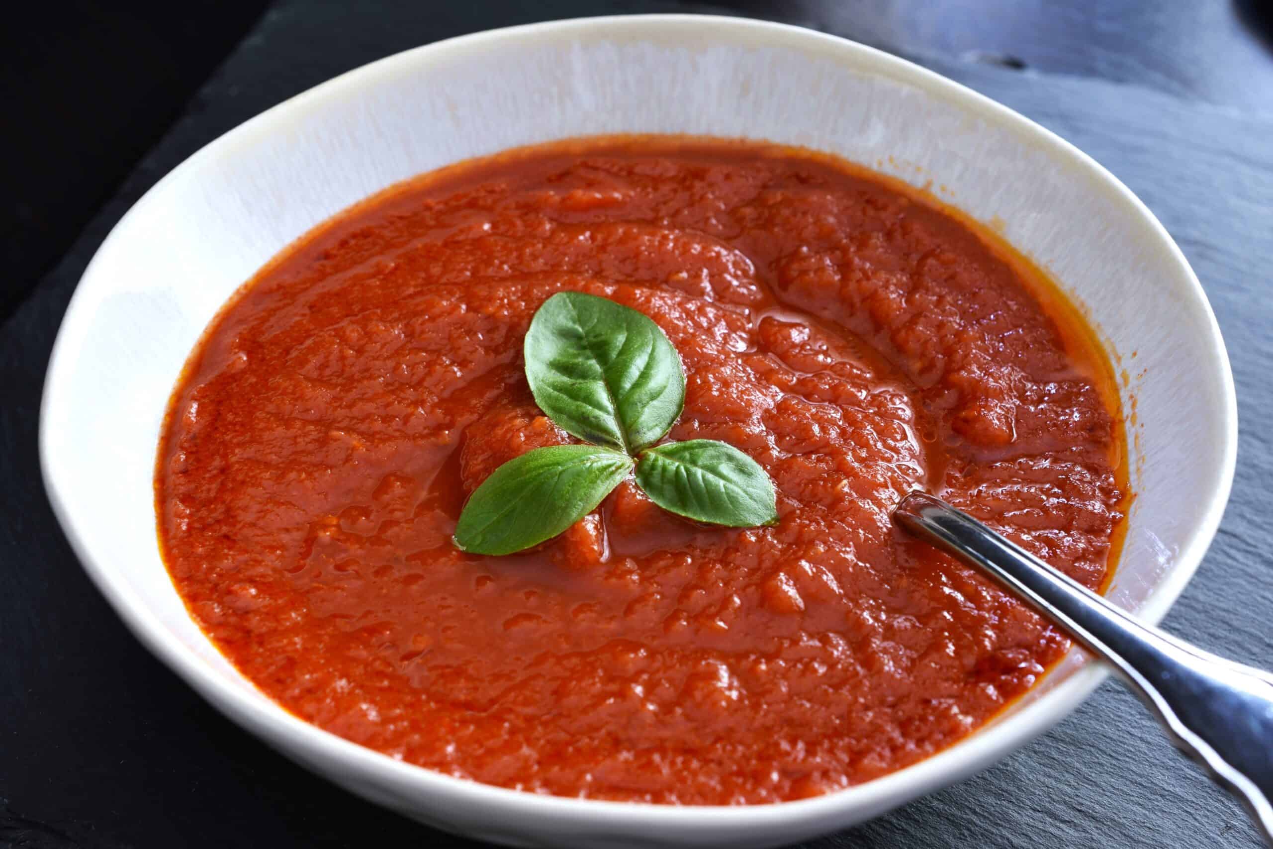 A bowl of fresh tomato pasta sauce with fresh basil garnish in a white bowl with a spoon.