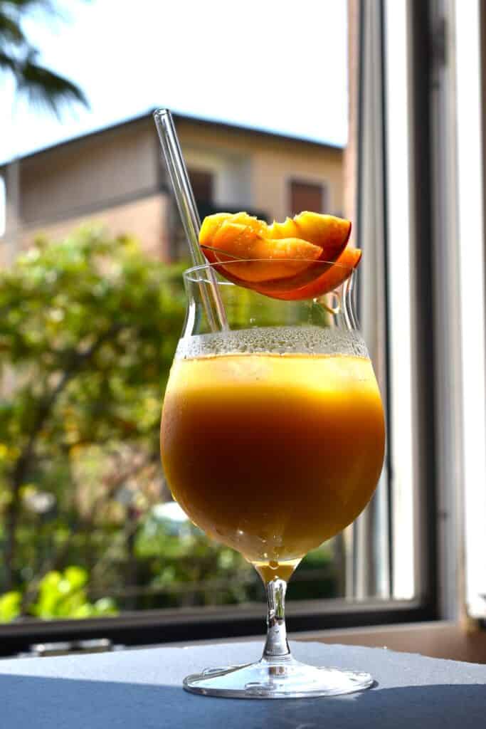 A glass of pick-me-up fruit cocktail with a glass straw and a garnish of fresh fruit, in front of an open window.