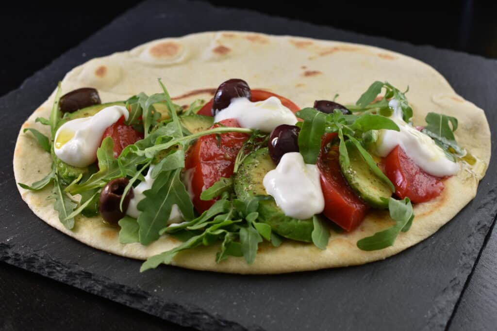 A piadina with avocado, tomato, vegan stracchino, rocket and olives.