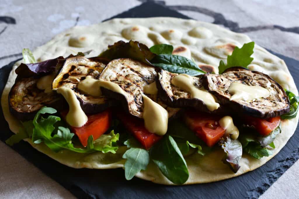 A piadina (Italian flatbread) with a vegan filling of grilled aubergines, tomatoes, mixed leaf salad, and mustard mayonnaise.