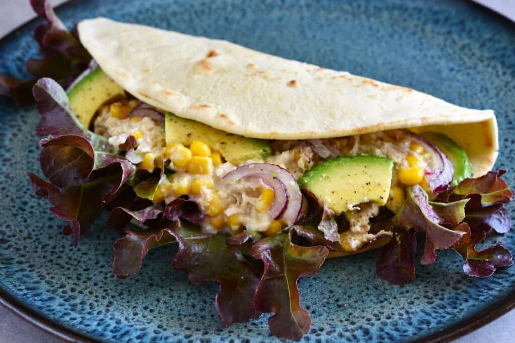 A vegan Italian flatbread piadina with vegan tuna mayonnaise, avocado, sweetcorn, red onion and lettuce.