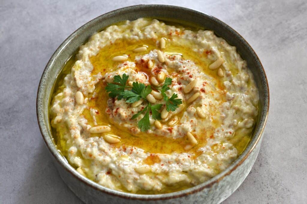 A bowl of vegan baba ganoush (moutabal) with a garnish of pine nuts, extra virgin olive oil, paprika and parsley.