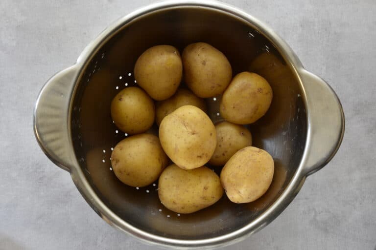 Boiled potatoes with their skins on steam drying in a colander.