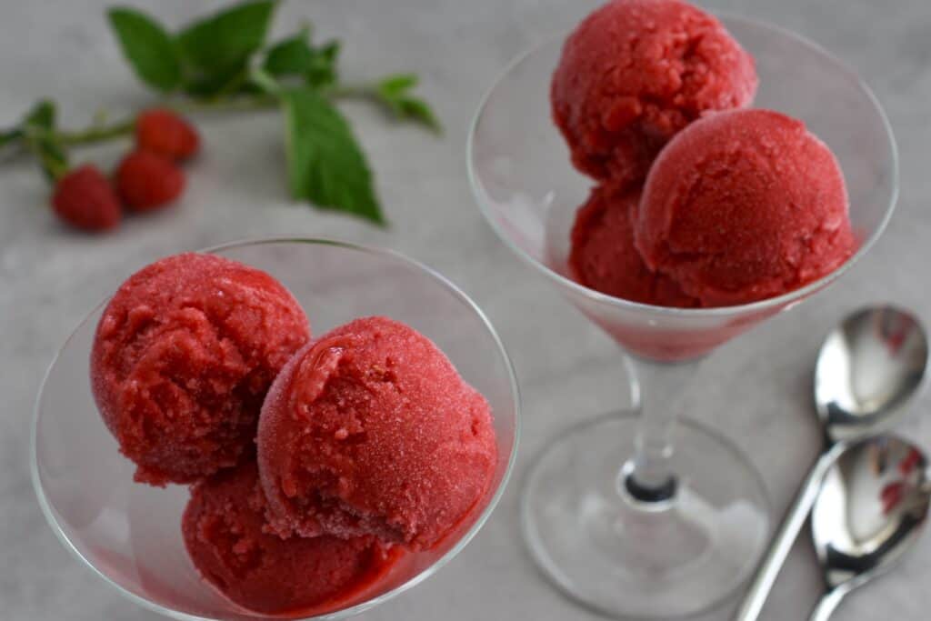 A close-up image of scoops of raspberry sorbet in cocktail glasses with spoons.