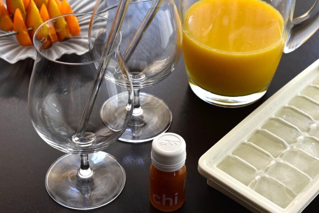 A jug of juice, ice cubes, Ringana chi, two glasses with glass straws and a garnish of fresh fruit.