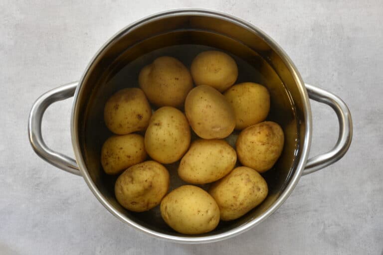 Potatoes with their skins on in a saucepan of cold water.