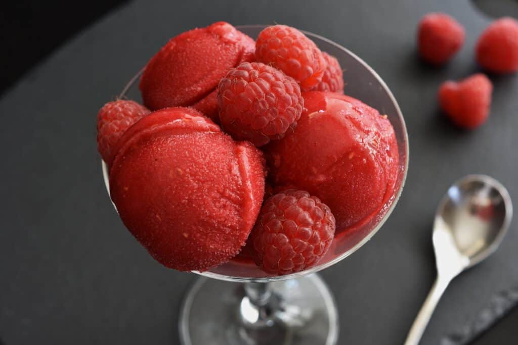 Raspberry sorbet in a glass with fresh raspberries.