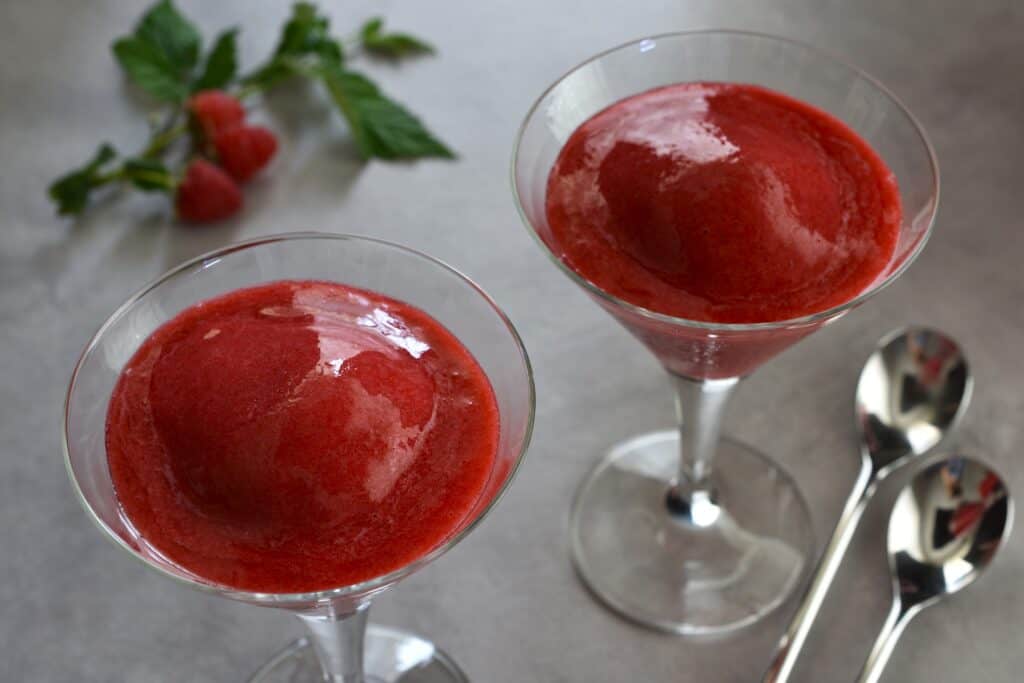 Two glasses of raspberry sorbet on a table with spoons.