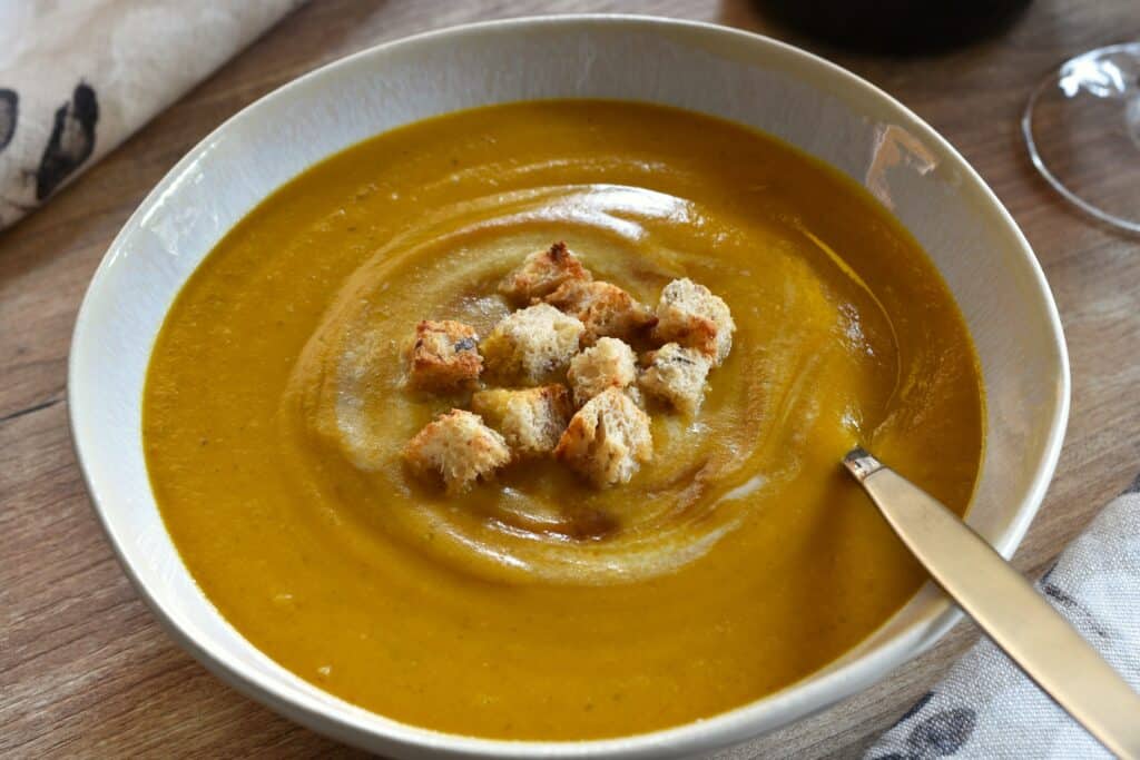 A bowl of pumpkin and red lentil soup with bread croutons.