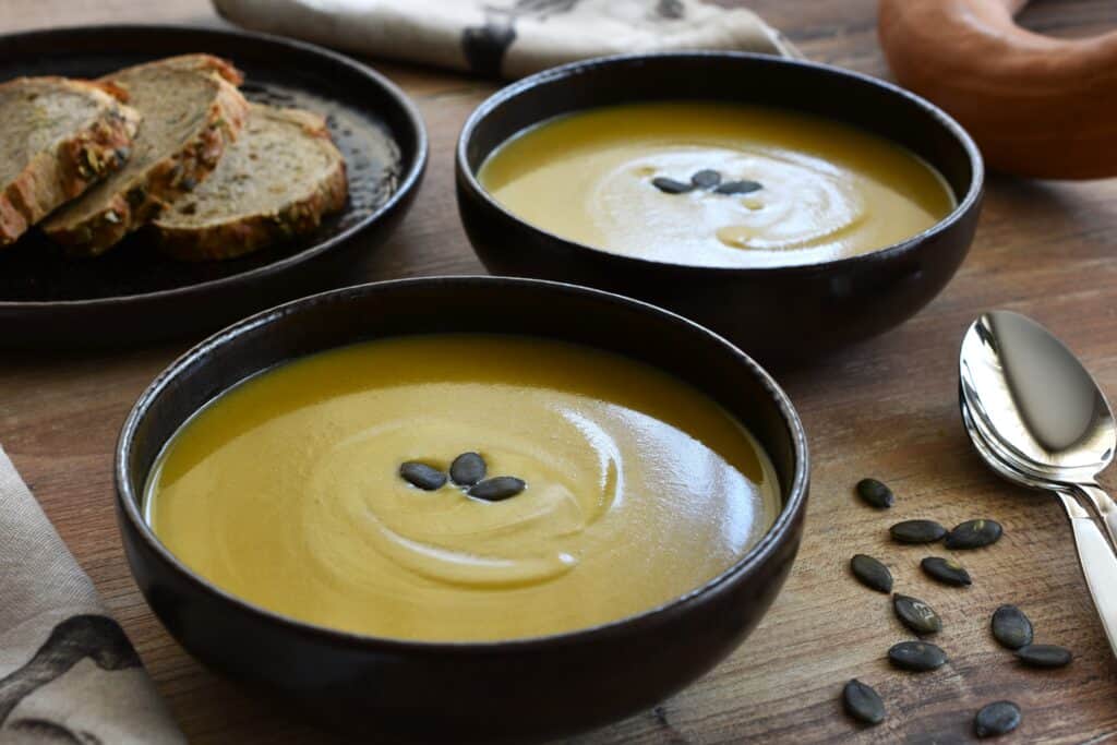 Two bowls of pumpkin and red lentil soup on a wooden table