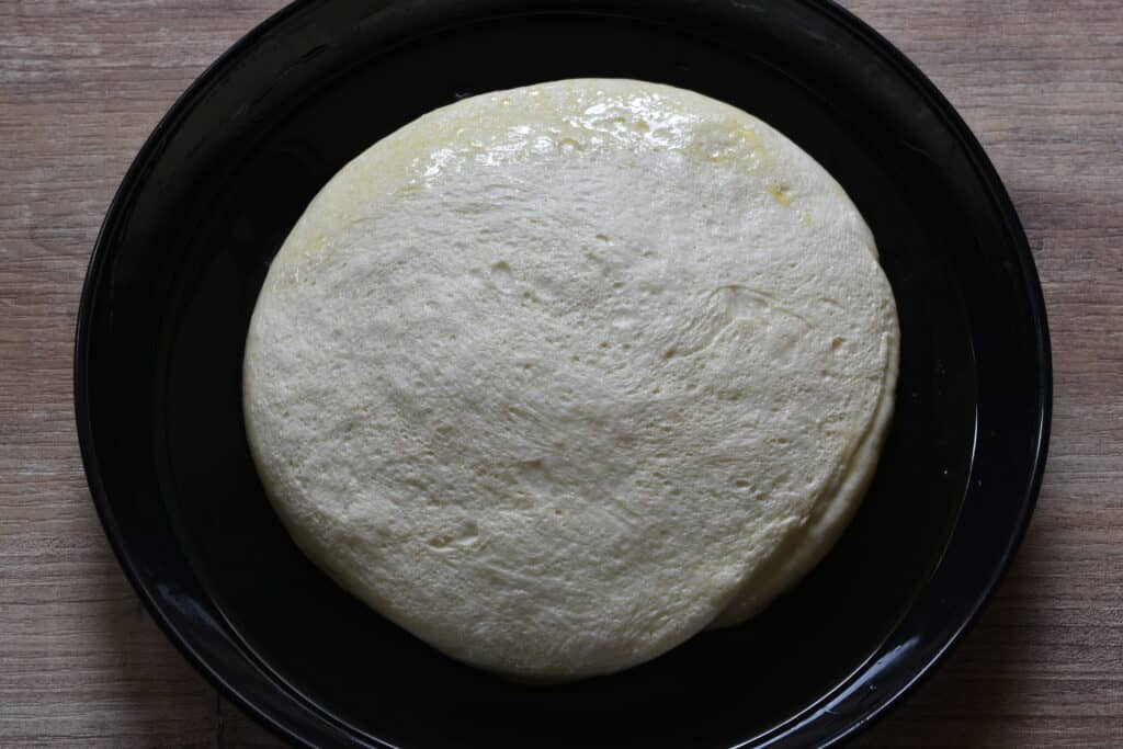 Focaccia dough after the first dough rise on an oiled tin.