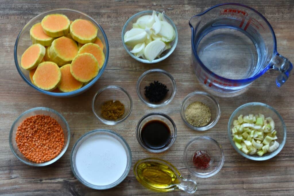 All the ingredients for pumpkin and red lentil soup laid out on a table in glass dishes.