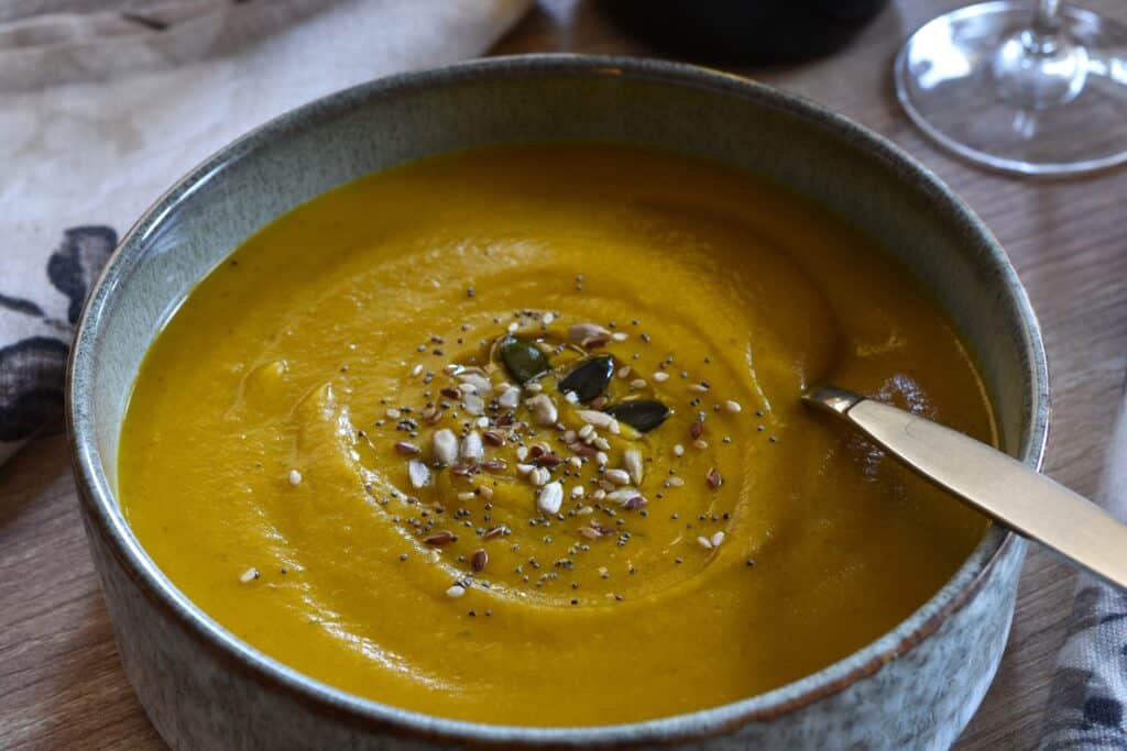 A bowl of pumpkin and red lentil soup garnished with mixed seeds. 