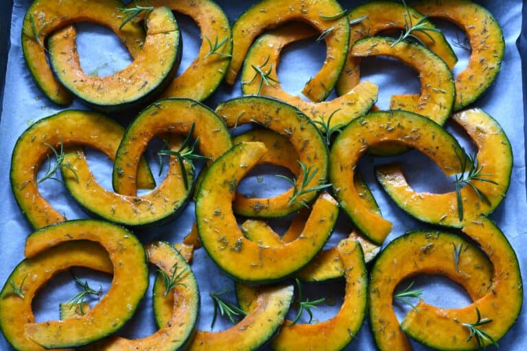 Pumpkin slices seasoned with herbs on a baking tray.