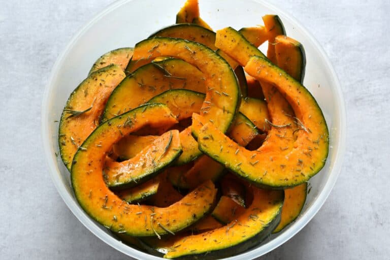 Pumpkin slices tossed in oil and herbs in a bowl.