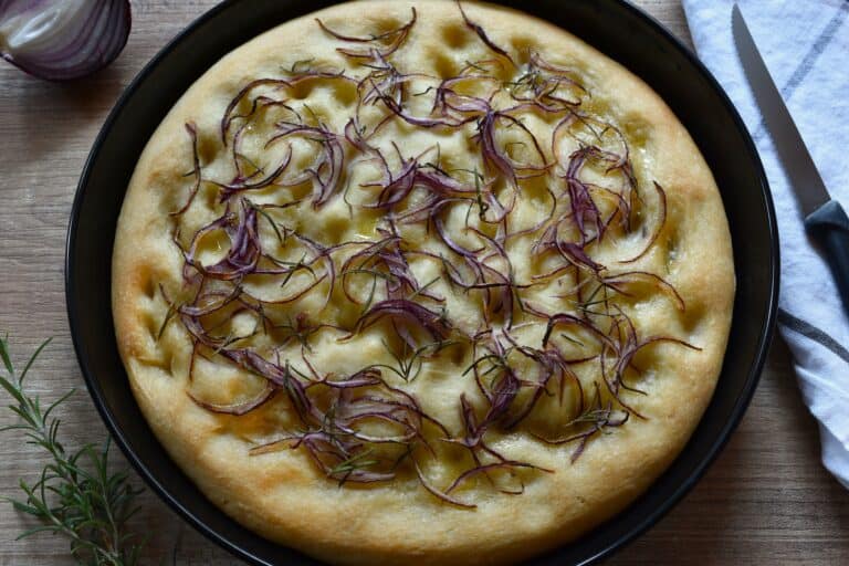 A whole red onion and rosemary focaccia on a table