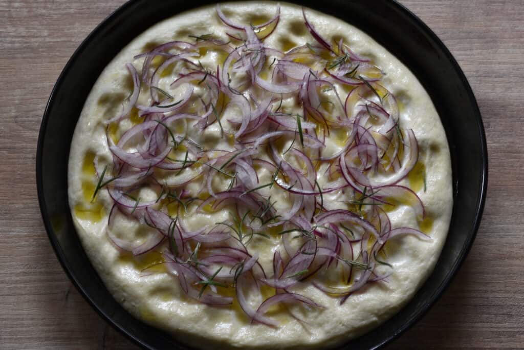 Focaccia dough with a topping of red onion and rosemary, just before going into the oven.