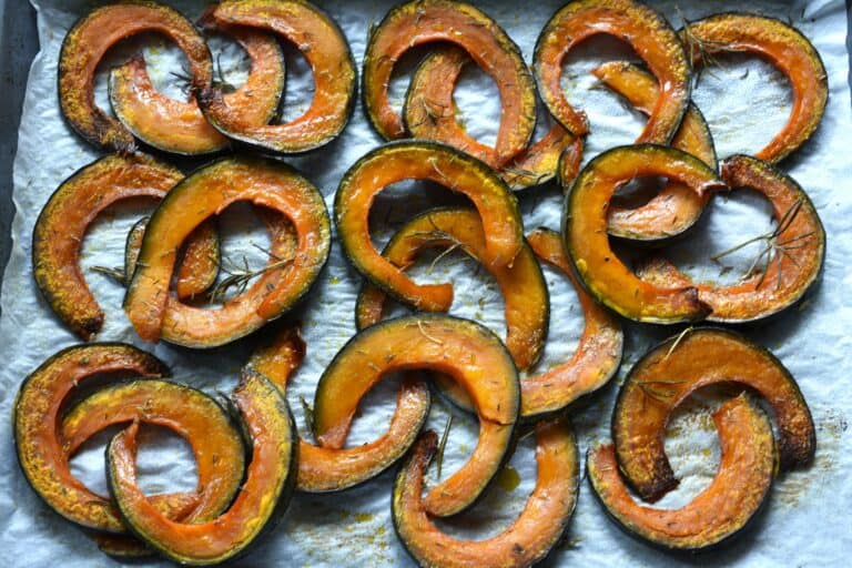 Roasted pumpkin slices with herbs on a baking tray.