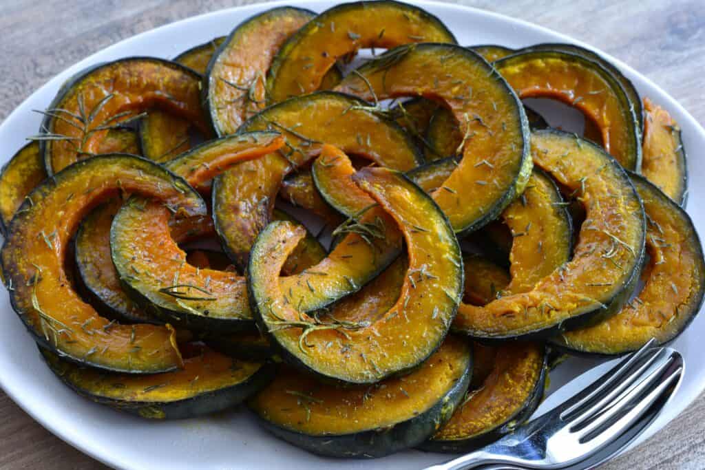 Roasted pumpkin slices with rosemary and thyme on an oval platter with a spoon and fork.