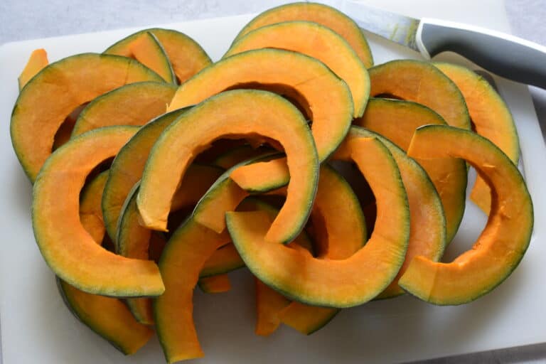 Slices of pumpkin on a chopping board with a knife.